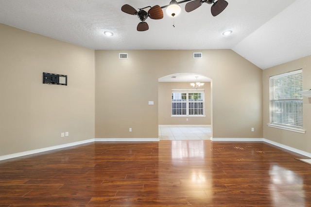 spare room with ceiling fan with notable chandelier, dark hardwood / wood-style flooring, lofted ceiling, and a textured ceiling