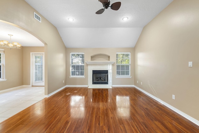 unfurnished living room with ceiling fan with notable chandelier, wood-type flooring, a textured ceiling, and vaulted ceiling