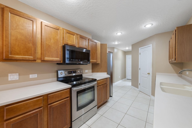 kitchen featuring sink, light tile patterned flooring, stainless steel appliances, and a textured ceiling