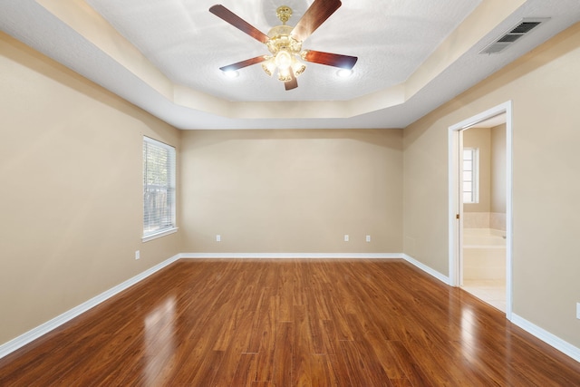 unfurnished room with hardwood / wood-style floors, ceiling fan, a textured ceiling, and a tray ceiling