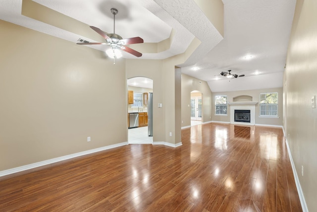 unfurnished living room with vaulted ceiling, ceiling fan, a textured ceiling, and light wood-type flooring