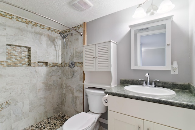 bathroom featuring vanity, toilet, tiled shower, and a textured ceiling