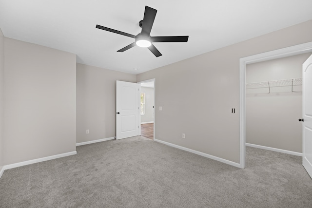 unfurnished bedroom featuring ceiling fan, a spacious closet, light carpet, and a closet