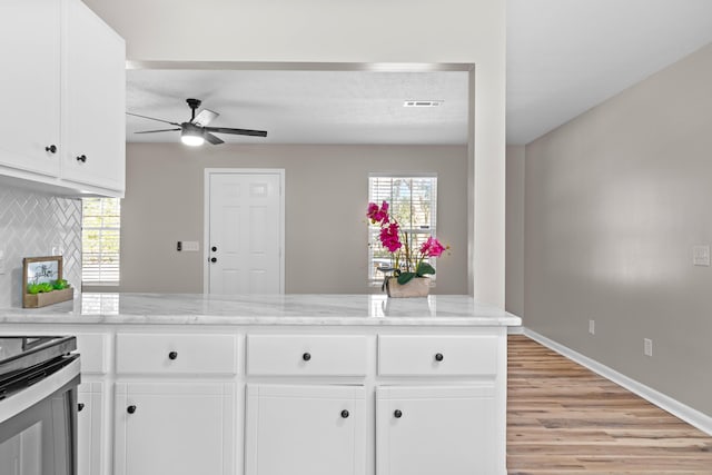 kitchen featuring kitchen peninsula, light stone countertops, white cabinetry, and backsplash