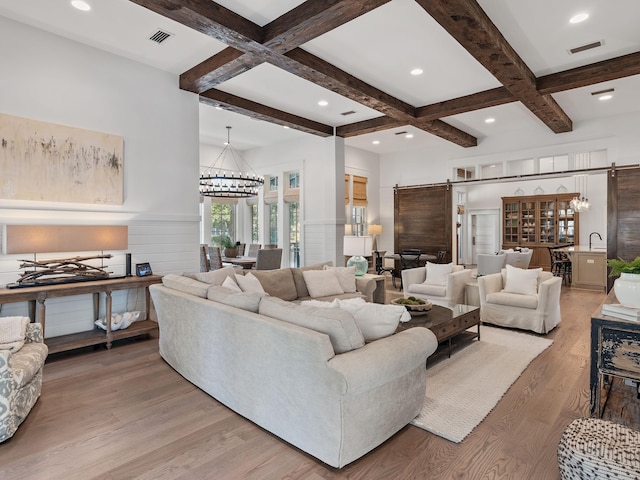 living room featuring beam ceiling, coffered ceiling, a barn door, hardwood / wood-style floors, and a chandelier