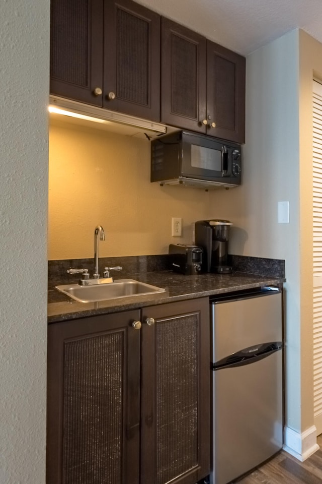 bar with stainless steel fridge, sink, wood-type flooring, and dark brown cabinets