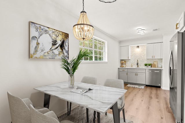 dining room featuring light hardwood / wood-style floors, crown molding, sink, and an inviting chandelier