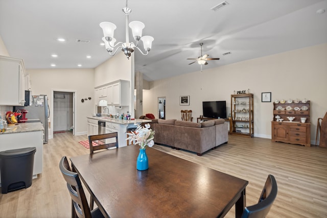 dining space featuring ceiling fan with notable chandelier, light wood-type flooring, sink, and vaulted ceiling