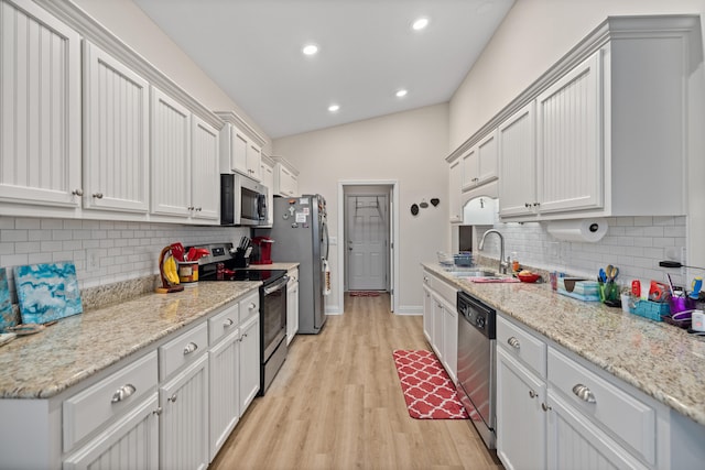 kitchen featuring appliances with stainless steel finishes, backsplash, vaulted ceiling, white cabinets, and light hardwood / wood-style floors