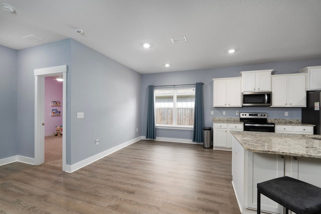 kitchen with stainless steel appliances, a kitchen breakfast bar, white cabinets, and light stone counters