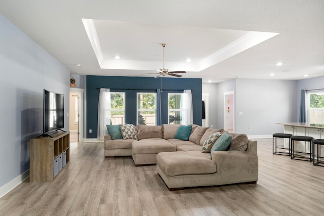 living room with light hardwood / wood-style floors, a raised ceiling, and ceiling fan