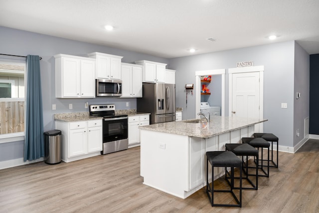 kitchen with stainless steel appliances, light stone countertops, a center island with sink, and white cabinets