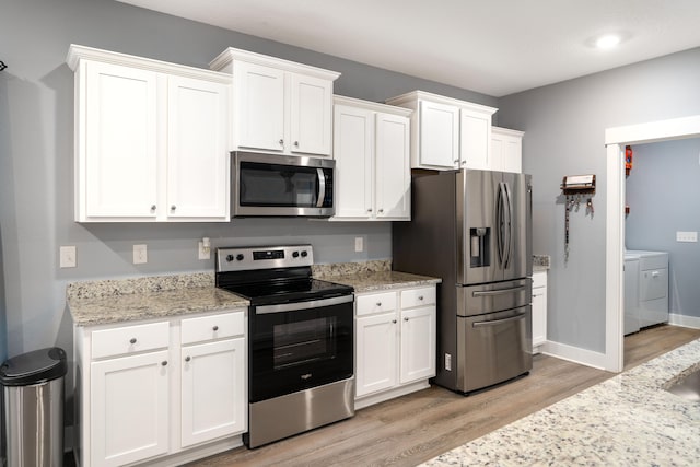 kitchen featuring white cabinetry, stainless steel appliances, light stone countertops, washing machine and clothes dryer, and light wood-type flooring