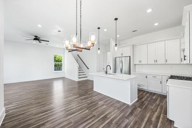 kitchen with pendant lighting, dark hardwood / wood-style floors, white cabinetry, stainless steel refrigerator, and an island with sink