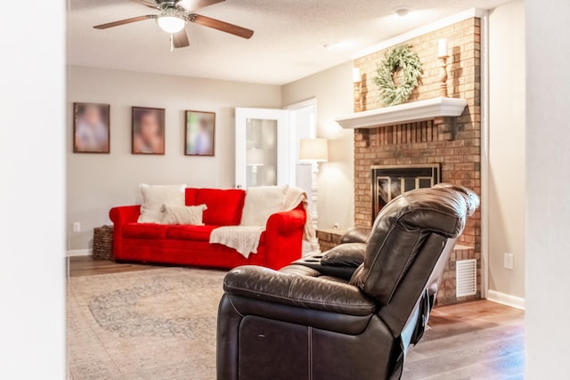 living room featuring ceiling fan, light hardwood / wood-style floors, a textured ceiling, and a brick fireplace