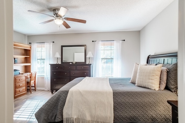 bedroom with multiple windows, ceiling fan, light hardwood / wood-style flooring, and a textured ceiling