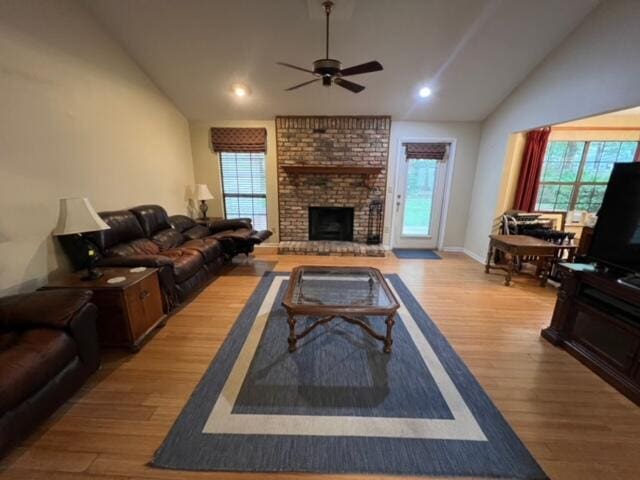 living room with a brick fireplace, light hardwood / wood-style flooring, ceiling fan, and lofted ceiling