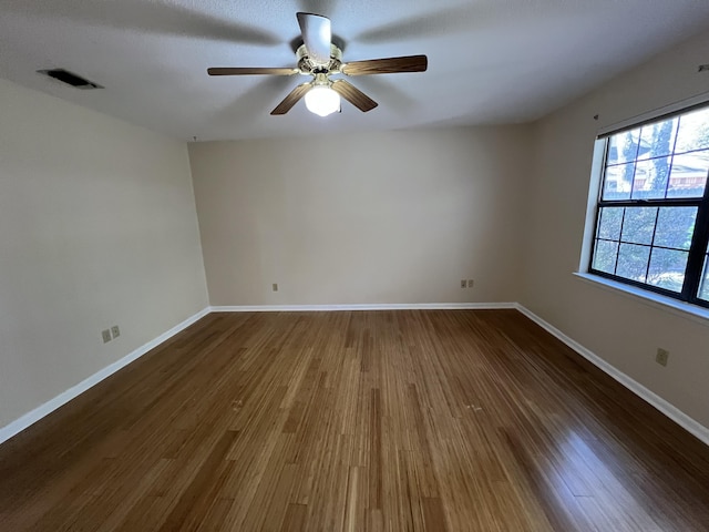 spare room with dark wood-style floors, a ceiling fan, visible vents, and baseboards