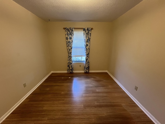 empty room with dark wood-style floors, a textured ceiling, and baseboards