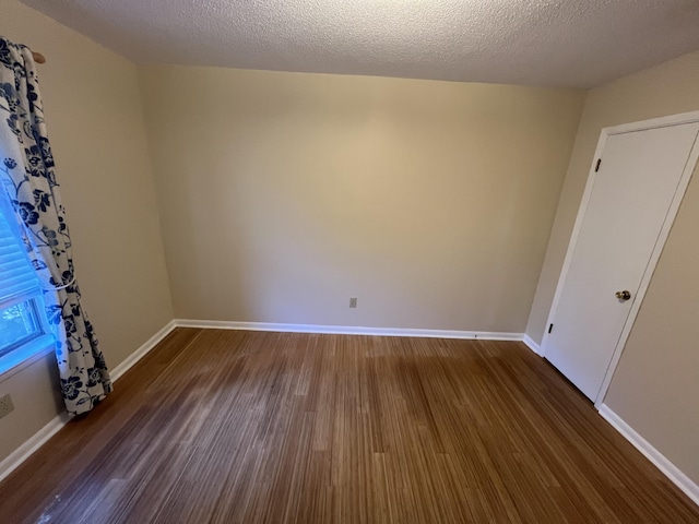 empty room with dark wood-style floors, baseboards, and a textured ceiling