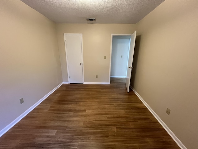 unfurnished room featuring dark wood-style floors, visible vents, a textured ceiling, and baseboards