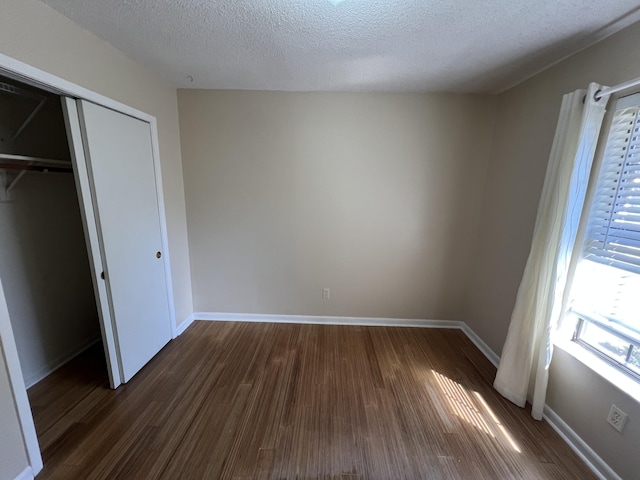 unfurnished bedroom with a textured ceiling, dark wood-type flooring, a closet, and baseboards