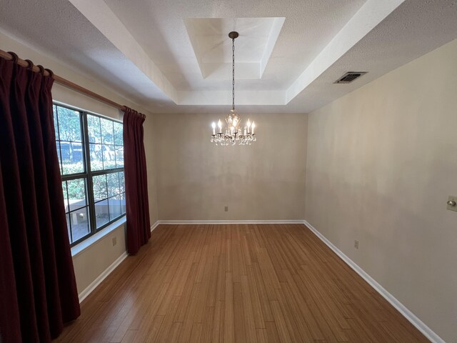 empty room with baseboards, visible vents, a tray ceiling, and wood finished floors