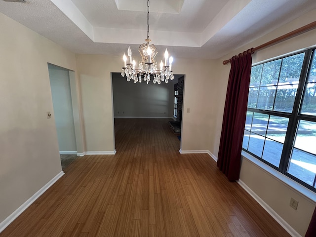 unfurnished dining area featuring an inviting chandelier, baseboards, a tray ceiling, and dark wood finished floors