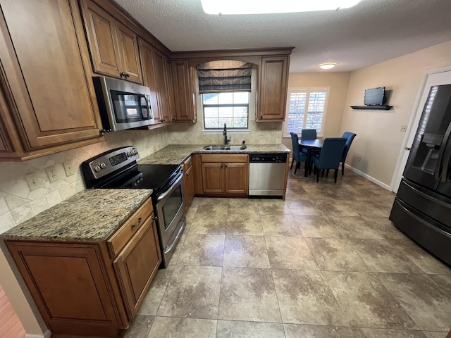 kitchen featuring stone countertops, stainless steel appliances, a sink, baseboards, and decorative backsplash