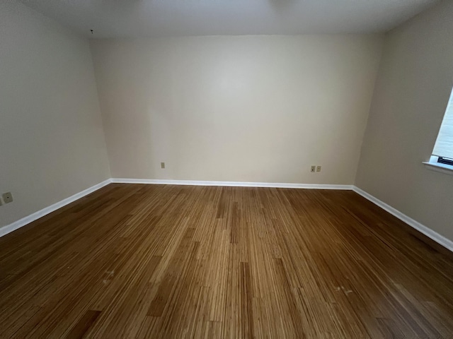 spare room with baseboards and wood finished floors