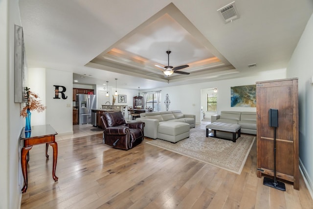 living room with a tray ceiling, light hardwood / wood-style flooring, and ceiling fan