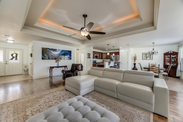 living room featuring ceiling fan with notable chandelier, ornamental molding, a raised ceiling, and light wood-type flooring