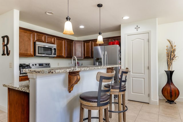 kitchen with light stone counters, decorative light fixtures, a breakfast bar area, and stainless steel appliances