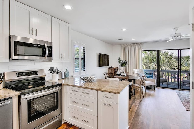 kitchen with white cabinets, hardwood / wood-style flooring, ceiling fan, light stone countertops, and appliances with stainless steel finishes