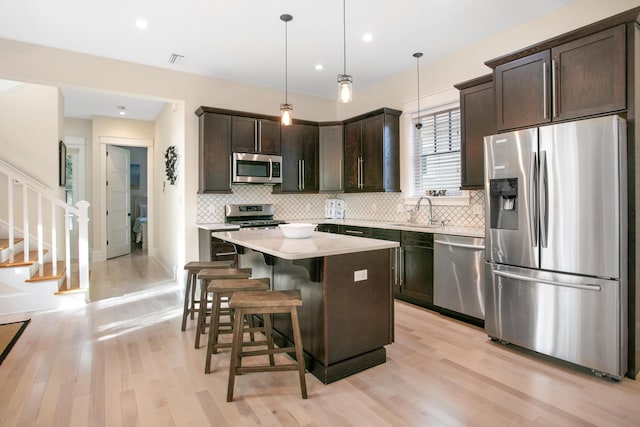 kitchen with light hardwood / wood-style flooring, a kitchen island, decorative light fixtures, and appliances with stainless steel finishes