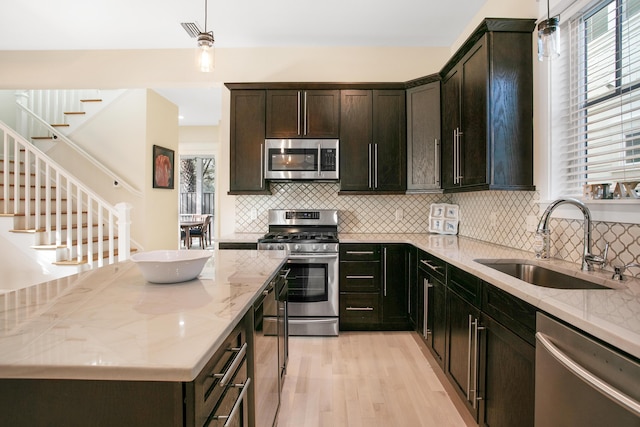 kitchen with light stone countertops, stainless steel appliances, sink, decorative light fixtures, and light hardwood / wood-style flooring