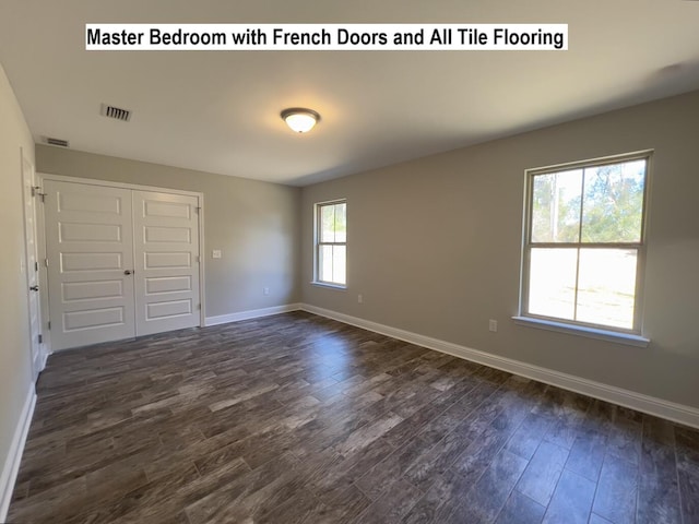 spare room with dark wood finished floors, visible vents, and baseboards