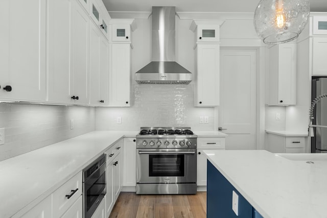 kitchen featuring white cabinets, appliances with stainless steel finishes, decorative light fixtures, and wall chimney exhaust hood