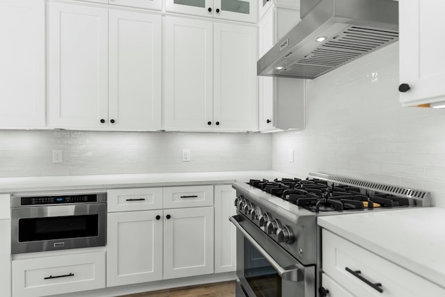 kitchen featuring white cabinets, wall chimney range hood, stainless steel appliances, and tasteful backsplash