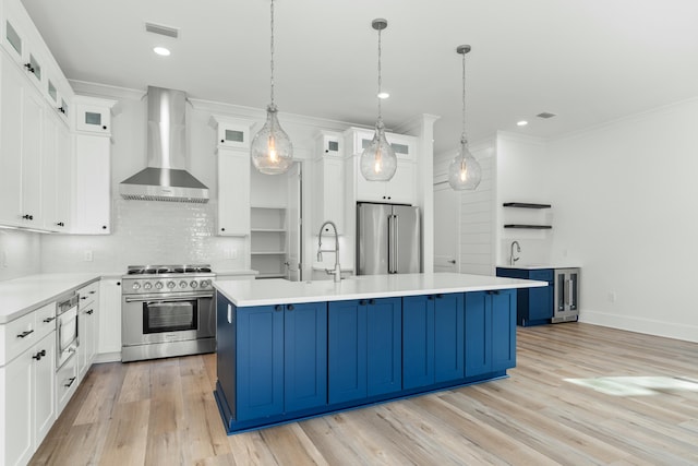 kitchen with white cabinets, premium appliances, a center island with sink, and wall chimney exhaust hood