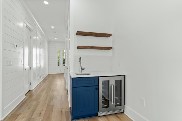 bar with light wood-type flooring, wine cooler, blue cabinets, and sink