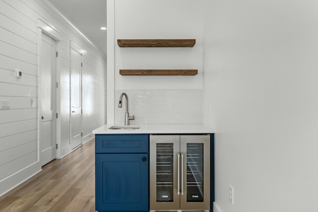 bar featuring tasteful backsplash, beverage cooler, sink, blue cabinetry, and light hardwood / wood-style floors