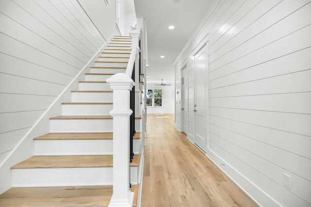 stairway with ceiling fan, hardwood / wood-style floors, and wood walls