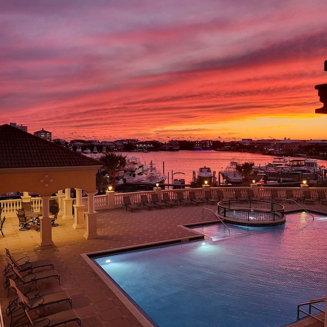 pool at dusk featuring a water view and a patio area