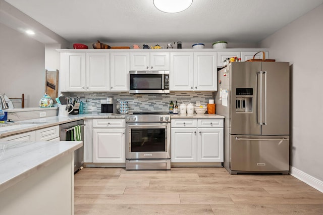 kitchen with white cabinets, light stone countertops, stainless steel appliances, and light hardwood / wood-style flooring