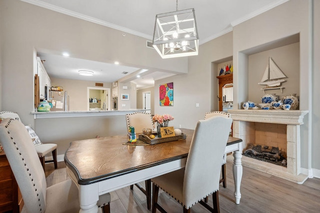 dining space featuring crown molding, a fireplace, light hardwood / wood-style floors, and a notable chandelier