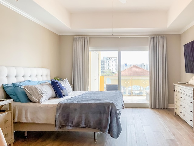 bedroom with a tray ceiling, access to outside, light wood finished floors, and crown molding