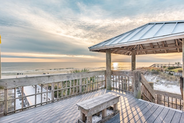 deck at dusk with a view of the beach, a gazebo, and a water view