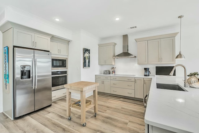 kitchen featuring appliances with stainless steel finishes, sink, wall chimney range hood, pendant lighting, and light hardwood / wood-style floors