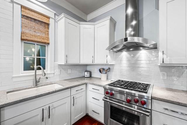 kitchen with light stone counters, premium range, sink, wall chimney range hood, and white cabinetry